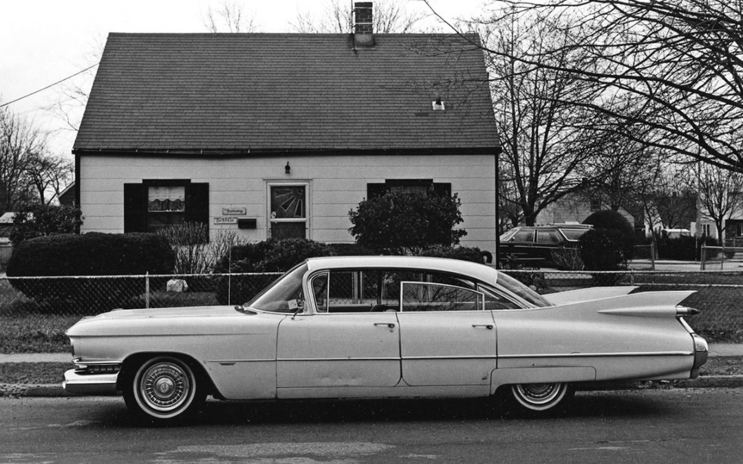 black and white picture of a Cadillac car in front of a Levitt style house